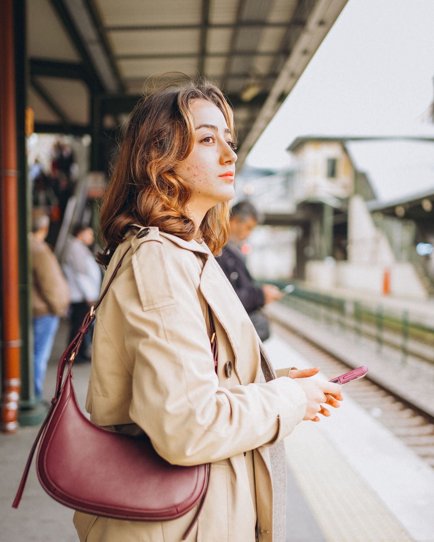 Une femme en trench attend son train sur le quai.